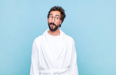 Genç sakallı bir adam banyo cübbesi giyiyor mutlu düşünceler ve fikirler düşünüyor, hayal kuruyor, kenarda yer arıyor.