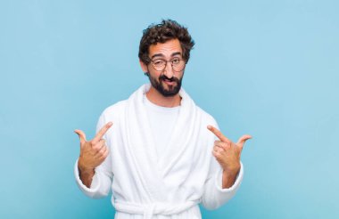 Genç sakallı bir adam kötü tavırlı, gururlu ve agresif görünümlü, yukarıyı gösteren ya da ellerle alay eden bir bornoz giyiyor.