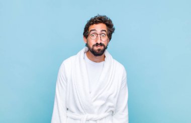 Genç sakallı bir adam banyo cübbesi giyiyor. Şapşal, çılgın, şaşkın bir yüz ifadesi var. Yanakları şişmiş, şişman ve yemek dolu.