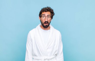 Genç sakallı bir adam banyo cübbesi giyiyor. Dehşete kapılmış ve şok olmuş hissediyor.