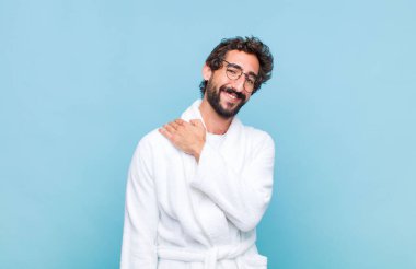 Banyo bornozu giymiş genç sakallı bir adam neşeli ve kendinden emin bir şekilde gülüyor.