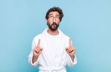 Banyo bornozu giymiş genç sakallı bir adam. Korkmuş ve ağzı açık. Şok olmuş ve şaşırmış bir şekilde yukarı bakıyor.