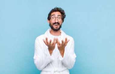 Banyo bornozu giyen genç sakallı adam umutsuz ve hayal kırıklığına uğramış, stresli, mutsuz ve sinirli, bağırıyor ve çığlık atıyor.