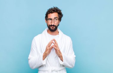 Genç sakallı bir adam banyo cübbesi giyiyor entrikalar ve komplolar kuruyor, hilekârlıklar ve hilekârlıklar düşünüyor, kurnaz ve ihanet ediyor.