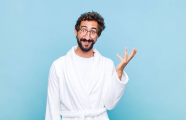 Banyo bornozu giyen genç sakallı adam mutlu, şaşırmış ve neşeli hissediyor, olumlu bir tavırla gülümsüyor, bir çözüm ya da fikri fark ediyor.