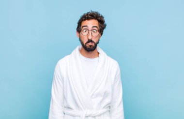 Banyo bornozu giyen genç sakallı adam şapşal ve komik görünüyor. Şaşı bakışlı, şakacı ve şakacı bir ifade.