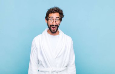 Banyo bornozu giyen genç sakallı adam mutlu ve hoş bir şekilde şaşırmış görünüyor. Büyüleyici ve şok edici bir ifadeyle heyecanlanıyor.