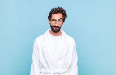 Banyo bornozu giyen genç sakallı adam kafası karışık ve şüpheli hissediyor, merak ediyor ya da karar vermeye çalışıyor.