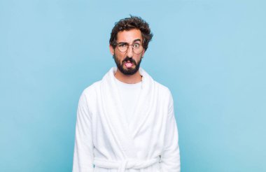 Banyo bornozu giymiş genç sakallı bir adam, tiksinti ve tedirginlik duyuyor, dilini dışarı çıkarıyor, iğrenç ve iğrenç bir şeyden hoşlanmıyor.