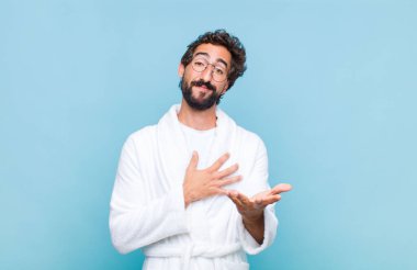 Genç sakallı bir adam banyo cübbesi giyiyor mutlu ve aşık, bir eli kalbinin yanında gülümsüyor ve diğer eli önde uzanıyor.