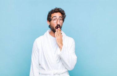 Genç sakallı bir adam banyo cübbesi giyiyor. Sabahın erken saatlerinde tembelce esniyor, uykulu, yorgun ve sıkkın görünüyor.