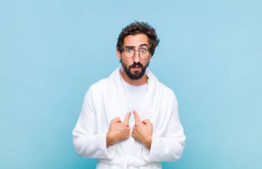Banyo bornozu giymiş genç sakallı bir adam şaşkın ve tuhaf bir bakışla kendini gösteriyor. Seçildiğime şaşırmış ve şaşırmış.