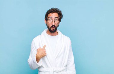 Banyo bornozu giymiş genç sakallı adam şaşkın, şaşkın ve güvensiz hissediyor, kendini göstererek kim olduğunu soruyor, ben mi??