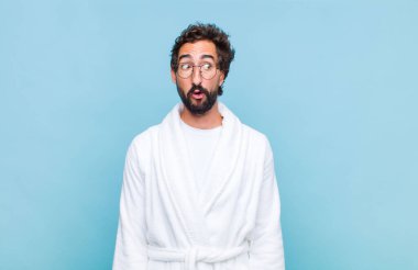 Banyo bornozu giyen genç sakallı adam şok olmuş, mutlu, şaşkın ve şaşırmış hissediyordu.