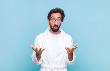 Banyo bornozu giyen genç sakallı adam son derece şaşırmış, şaşırmış, endişeli ve paniklemiş, stresli ve dehşete kapılmış bir bakışla