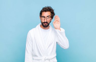 Banyo bornozu giymiş genç sakallı adam ciddi ve meraklı görünüyor, dinliyor, gizli bir konuşma veya dedikodu duymaya çalışıyor, gizlice dinliyor.