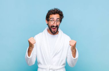 Banyo cübbesi giyen genç sakallı adam mutlu, pozitif ve başarılı hissediyor zaferi, başarıları ya da iyi şansı kutluyor.