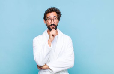 Genç sakallı bir adam banyo cübbesi giyiyor düşünceli, meraklı ya da hayal kuruyor, hayal kuruyor ve mekanı kopyalamak için yukarı bakıyor.