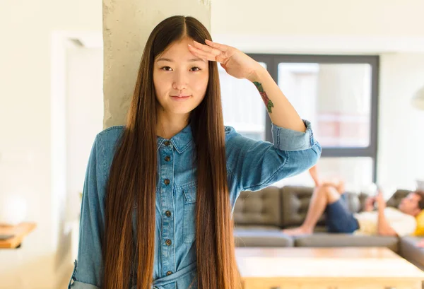 young pretty asian woman greeting the camera with a military salute in an act of honor and patriotism, showing respect