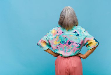 Orta yaşlı havalı bir kadın kafası karışık ya da dolu ya da şüphe ve soru dolu, merak ediyor, elleri kalçasında, dikiz aynasından.