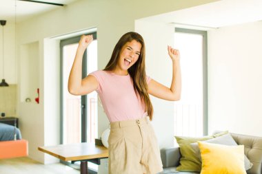 Genç ve güzel bir kadın muzaffer bir şekilde bağırıyor. Heyecanlı, mutlu ve şaşırmış görünüyor. Kutlama yapıyor.