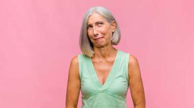 Orta yaşlı, güzel bir kadın mutsuz, korkmuş ya da endişeli görünüyor ağzı sonuna kadar açık ve iki kulağını da elleriyle kapatıyor.