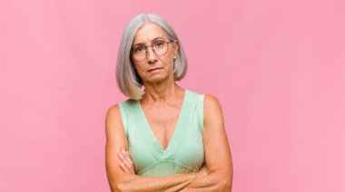 Orta yaşlı, güzel bir kadın bilgisiz ve kafası karışık, bir çözüm düşünüyor, eli kalçasında, diğeri kafasında, dikiz aynasından.