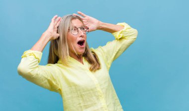 Orta yaşlı, güzel bir kadın mutlu, gururlu ve tatmin olmuş görünüyor. Kollarını kavuşturup gülümsüyor.