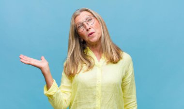 Orta yaşlı, güzel bir kadın şaşkın ve şaşırmış hissediyor, gülümsüyor, el ele tutuşuyor, mutlu ya da şükran duyuyor.