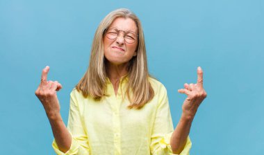 Orta yaşlı, güzel bir kadın kendini mutlu, pozitif ve başarılı hissediyor. Göğsünde el yapımı V şekli var. Zafer ya da huzur gösteriyor.