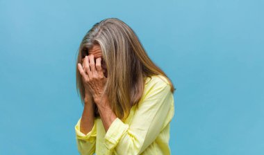 Orta yaşlı, güzel bir kadın elleri ile ağzını kapatıyor, şok olmuş, şaşırmış bir ifadeyle, sır saklıyor ya da 