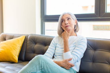 Orta yaşlı, güzel bir kadın mutlu bir şekilde gülümsüyor ve hayal kuruyor ya da şüphe ediyor.