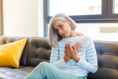 Orta yaşlı güzel bir kadın üzgün, yaralı ve kalbi kırık görünüyor, iki elini de kalbe yakın tutuyor, ağlıyor ve bunalımda.