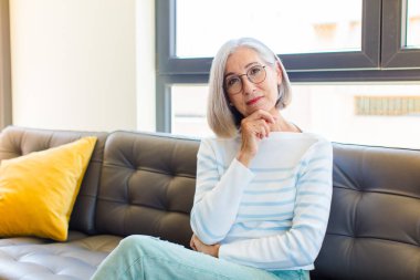 Orta yaşlı, güzel bir kadın ciddi görünüyor, kafası karışık, kararsız ve düşünceli, seçenekler ve seçenekler arasında şüpheci.