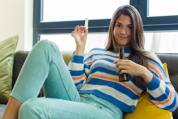 Genç ve güzel bir kadın birasını evinde, koltuğunda oturuyor.