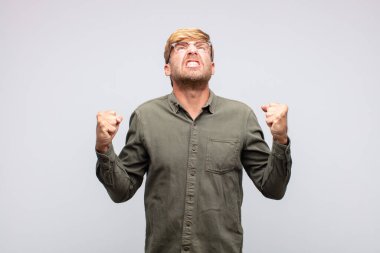 Genç sarışın adam kızgın bağırıyor.