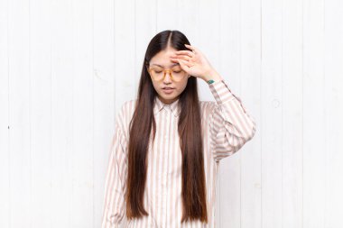 Asyalı genç kadın stresli, yorgun ve hayal kırıklığına uğramış görünüyor, alnından ter akıyor, umutsuz ve bitkin hissediyor.