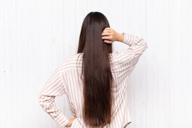 Asyalı genç kadın düşünüyor ya da şüphe ediyor, kafasını kaşıyor, kafası karışık ve kafası karışık hissediyor, arkaya ya da arkaya bakıyor.