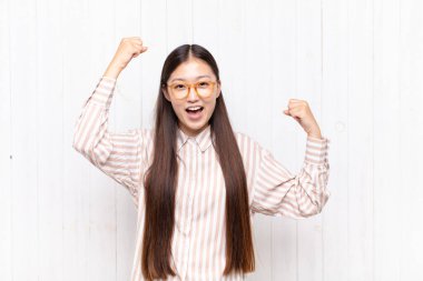 Asyalı genç bir kadın muzaffer bir şekilde bağırıyor. Heyecanlı, mutlu ve şaşkın bir kazanan gibi görünüyor.