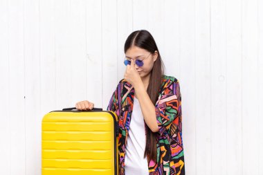 Asyalı genç bir kadın stresli, mutsuz ve hayal kırıklığına uğramış, alınına dokunmuş ve şiddetli baş ağrısı çeken. tatil kavramı