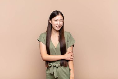 Asyalı genç bir kadın utangaç ve neşeli bir şekilde gülüyor, arkadaş canlısı, olumlu ama güvensiz bir tavırla.