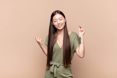 Asyalı genç kadın gülümsüyor, kaygısız hissediyor, rahat ve mutlu, dans ediyor ve müzik dinliyor, bir partide eğleniyor.