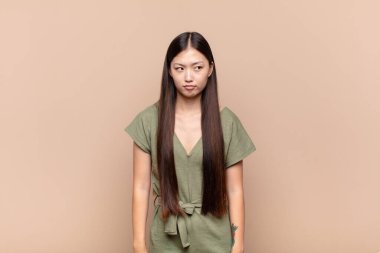 Asyalı genç bir kadın üzgün, üzgün ya da kızgın. Olumsuz bir tavır sergiliyor, anlaşmazlık içinde kaşlarını çatıyor.