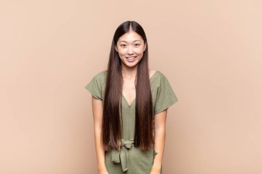 Asyalı genç kadın mutlu ve şapşal görünüyor. Geniş, eğlenceli, deli gülüşü ve gözleri açık.