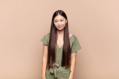 Asyalı genç kadın pozitif ve kendinden emin gülümsüyor. Tatmin olmuş, arkadaş canlısı ve mutlu görünüyor.