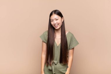 Asyalı genç bir kadın, büyük, dost canlısı, kaygısız bir gülümsemesi var, pozitif, rahat ve mutlu görünüyor, ürpertici.