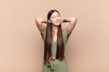 Asyalı genç bir kadın gülümsüyor ve rahatlıyor, tatmin oluyor ve kaygısızca gülüyor.