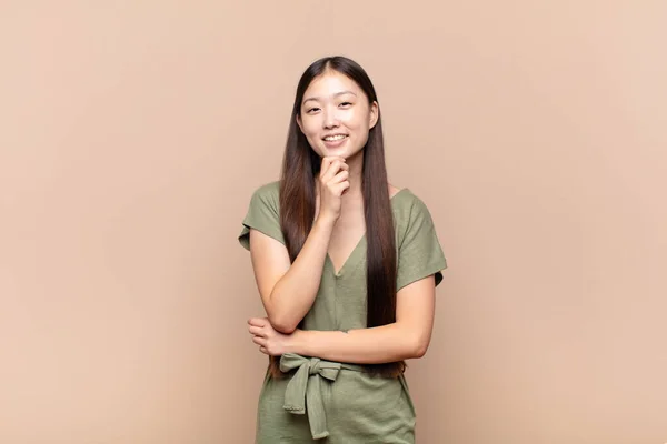 アジア系の若い女性はあごを手にして幸せそうな笑顔で質問をしたり選択肢を比較したり — ストック写真