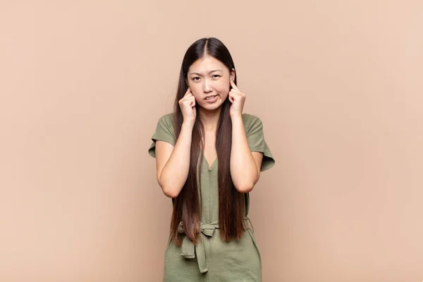 アジア系の若い女性は怒りとストレスといらいらを感じ耳の両方を耳の聞こえない音や音や大きな音楽で覆い — ストック写真