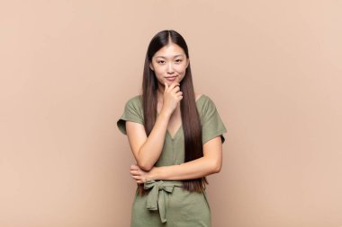 Asyalı genç kadın ciddi görünüyor, kafası karışık, kararsız ve düşünceli, seçenekler ve seçimler arasında şüpheci.